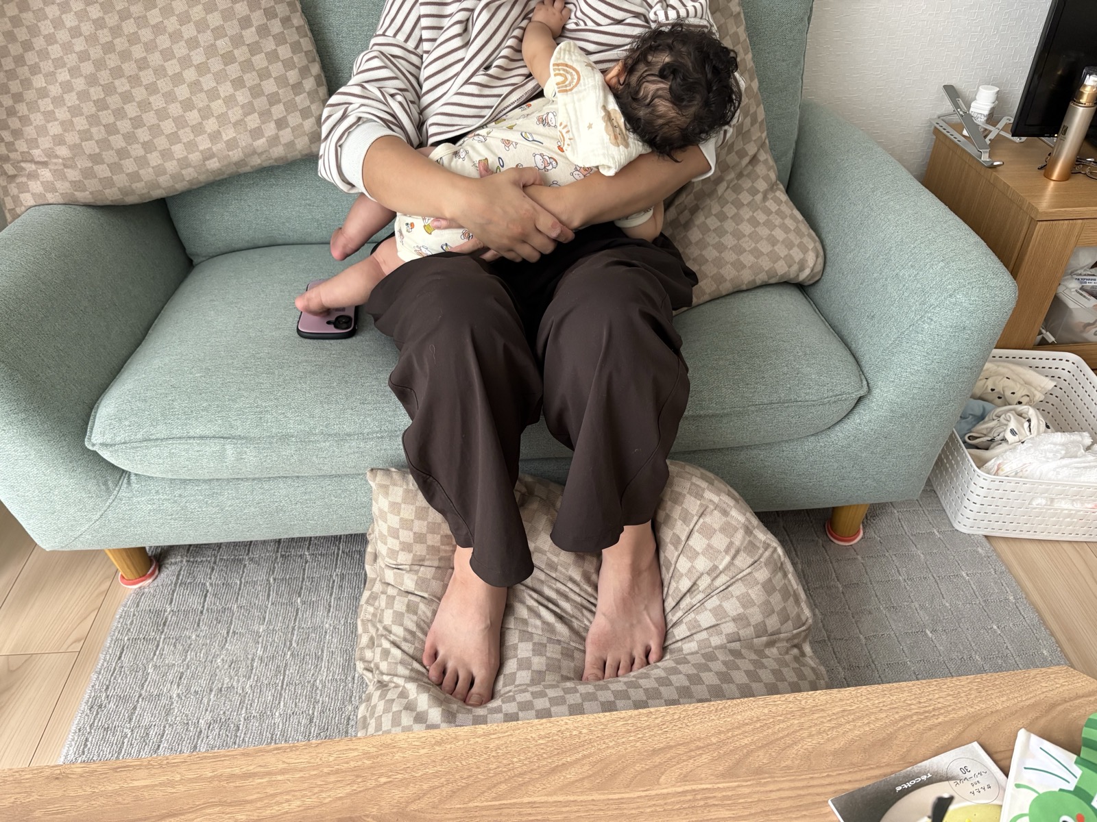 ソファに腰かけ、足元にクッションを置いて赤ちゃんを身体に寄せて授乳しているお母さんの姿勢